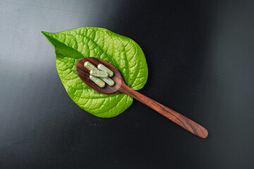 Wall Mural - Pile of herbal capsules on wooden spoon with herbs and green natural Betel pepper leaf background