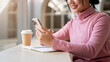 © bongkarn - A close-up of a smiling, positive Asian woman using her smartphone while sitting in a coffee shop.