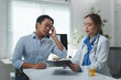 © Phimwilai - Doctor and patient engage in a consultation at a modern clinic. The doctor reviews medical information on a tablet, while the patient appears concerned. Medicine bottles are visible on the desk