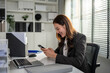 © Kawee - Asian happy businesswoman swiping on smartphone while working in office.