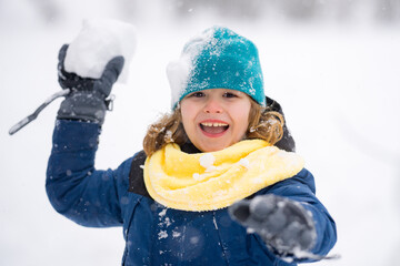 Wall Mural - Kid playing with Snowball snow during snowfall. Snowball fight. Kid in a warm clothes, hat, hand gloves and scarf playing Snowball. Snowy winter day for kids. Child snowball fight in snow.