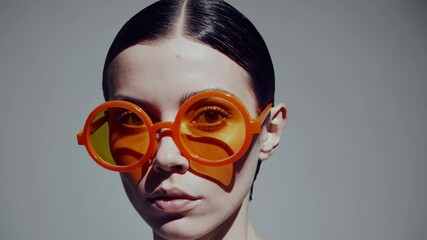 Aufkleber - a minimal portrait of a woman wearing oversized neon-orange round glasses against a pale background.
