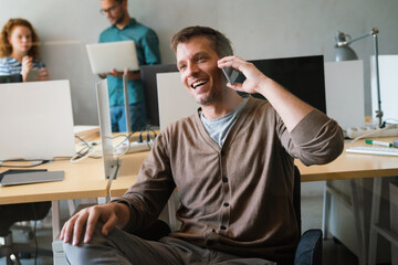 Wall Mural - Happy startup business man, programmer, freelancer discussing on mobile phone while looking away.