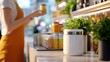 © Krittika - A woman in an apron holds a jar while standing beside a counter adorned with vibrant plants and organized containers.