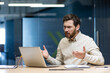 © Tetiana - Frustrated and sad young businessman man sitting at desk in office and talking on video call on laptop gesturing with hands