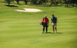 © Jacob Lund - Two male golfers walking together on a sunny fairway, carrying golf bags near a sand bunker