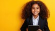 © velikiyzayats - A Confident Young Girl with Curly Hair Wearing a Suit, Smiling and Holding a Tablet Against a Bright Yellow Background
