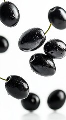 Wall Mural - Dark glossy berries falling against a white background. Water droplets are visible on their surface.  Close up view emphasizes texture and color