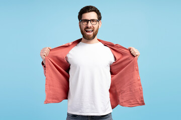 Bearded man in eyeglasses, screaming and showing white t shirt, posing at camera