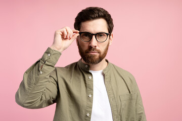 Wall Mural - Handsome man touching his eyeglasses, posing isolated over pink color background