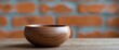 © AkuAku - Close-up of an empty wooden bowl with a smooth finish on a wooden surface against a blurred orange brick wall background.