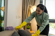 © Gybziii - A woman is cleaning a couch with a yellow glove on her left hand. She is smiling as she works
