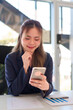 © snowing12 - Close-up of a young Asian businesswoman using a smartphone while working in a bright and modern office