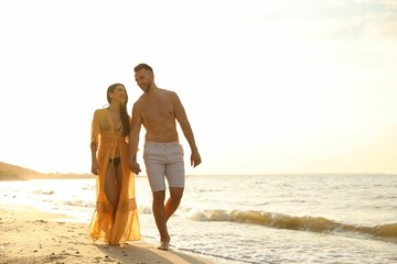 Wall Mural - Happy young couple walking together on beach at sunset