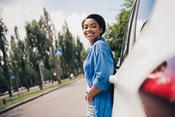 Wall Mural - Young woman smiling by her car in the city street during a sunny day, embracing summer vibes and modern urban style