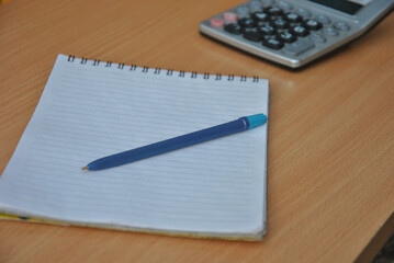 pen on a blank sheet of notepad and a blurry calculator in the background. business idea development