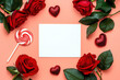 © PixPacks - Happy Valentine's Day greeting card and envelope, styled with Valentine red roses, heart shape gift and lipstick kissess chocolates on a modern coral background. Mockup. Top view flat lay. Copy space.