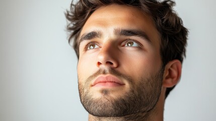 Wall Mural - minimalistic portrait of 30 years old brunette man with beard looks up on white background, male face