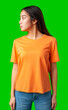 © fotofabrika - Young woman in an orange shirt poses confidently against a vibrant green background
