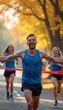 © natakot - A group of enthusiastic runners bursts through the finish line, their faces radiating pure joy against a backdrop of vibrant autumn foliage. The lead runner, a man in a blue tank top, beams with