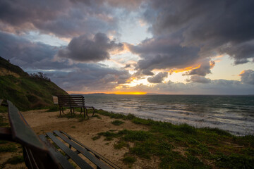 Wall Mural - Serene sunset over the ocean, viewed from a grassy clifftop with empty benches.