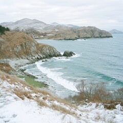 Wall Mural - Stunning Winter Coastal Landscape with Snowy Cliffs and Blue Ocean Waves in Scenic Placid Waters, Serene Snow-Capped Hills in Pristine Rugged Beauty, Cloudy Sky View