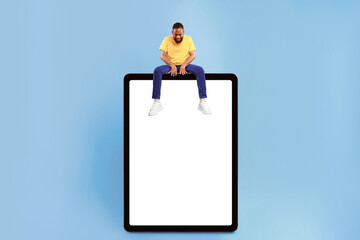 Wall Mural - attractive young african american guy sitting on top of giant tablet computer, looking down at empty
