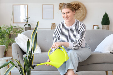 Wall Mural - Young woman watering green plant at home