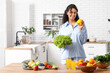 © Pixel-Shot - Young happy African-American woman with glasses of juice, different vegetables and fruits in kitchen. Independence from Meat Day
