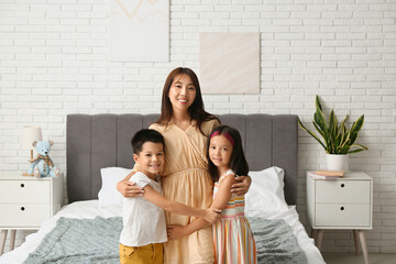 Wall Mural - Beautiful young happy Asian mother hugging with her cute little children in bedroom at home