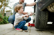 © MNStudio - Cute little boy helping his father to change car wheels at their backyard. Father teaching his little son to use tools.