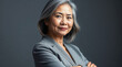 © adynue - Stylish confident adult 50 years old Asian female psychologist standing arms crossed looking at camera at gray background. Portrait of sophisticated grey hair woman advertising products and services