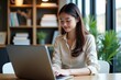 © SimpleDesignStudio - A Young Woman Working on a Laptop in a Bright, Stylish Home Office Environment Surrounded by Bookshelves and Greenery on a Productive Day