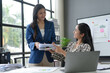 © amnaj - Businesswomen exchanging documents in modern office