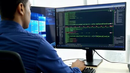 A man is working on a computer with two monitors, one of which is displaying a black screen