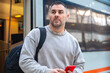 © alfons - Focused Man Holding Red Smartphone at Train Station