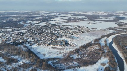 Wall Mural - Aerial view of Snow-covered farmlands with small neighborhood and winding river on a cloudy day