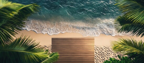 Sticker - Aerial view of a wooden deck on a sandy beach surrounded by lush green palm leaves with turquoise waves gently crashing in the background