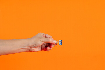 Wall Mural - Hand and colorful paperclip on orange background.