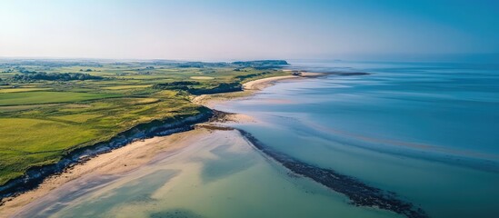 Aufkleber - Aerial view of a serene coastline with turquoise waters and green fields under a clear blue sky highlighting the beauty of nature's landscape