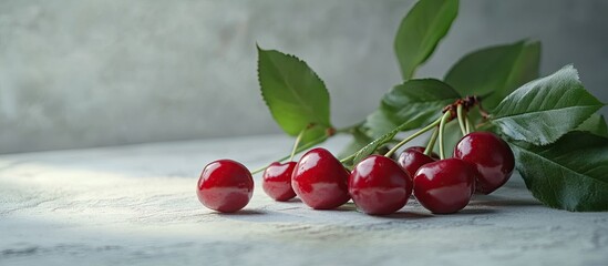 Fototapete - Fresh red cherries with green leaves arranged elegantly on a textured gray marble surface, soft natural light highlighting the glossy fruit.