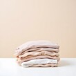 © ANASTASIIA - Minimalist stack of neutral toned sweatshirts on white surface against beige background