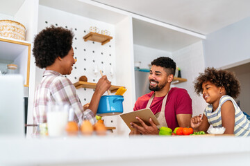 Wall Mural - Happy smiling african american parents enjoy weekend play with child in kitchen. Family love concept