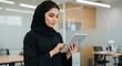 © Zubair - Confident Middle Eastern Businesswoman in Black Abaya and Hijab Using Tablet in Modern Office Setting