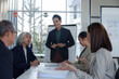 © crizzystudio - Young businessman leading a presentation to his diverse team during a meeting in a modern office, discussing work strategy and analyzing financial data