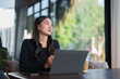 © crizzystudio - Young asian businesswoman is sitting at a table in a cafe, working on her laptop and enjoying a cup of coffee while contemplating her next business move