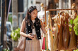 © crizzystudio - Stylish young woman holding her smartphone and choosing reusable shopping bags at an outdoor market stall, promoting sustainable and eco-conscious consumerism