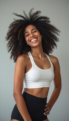 Canvas Print - A vibrant young woman with voluminous curly hair beams with joy, wearing a white sports bra and black shorts. Her infectious smile radiates positivity and confidence, embodying a spirit of health and