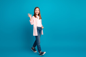 Wall Mural - Cheerful young girl smiling and waving against a bright blue background showcasing vibrant youthfulness and charm