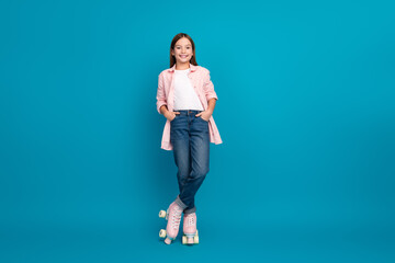 Wall Mural - Young girl wearing trendy casual outfit posing with roller skates on blue studio background